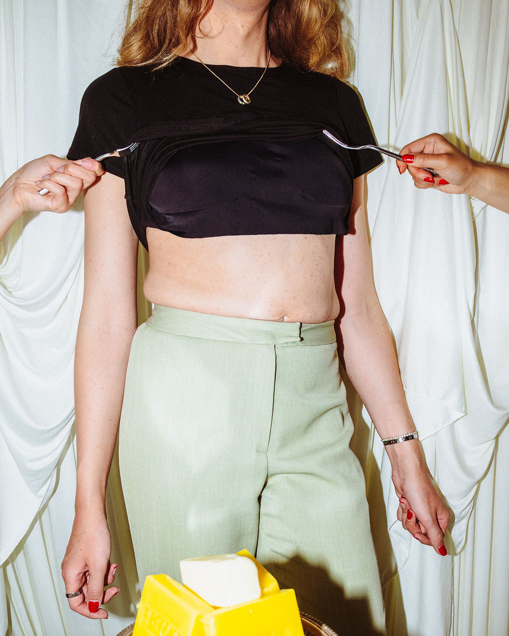 Person wearing a black crop top and green pants with a bowl of butter on a table.